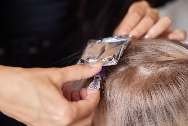 Il parrucchiere rende bouffant usando il pettine su ciocche sottili con la tecnica Shatush per schiarire i capelli