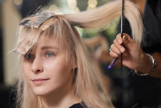 Il parrucchiere rende bouffant usando il pettine su ciocche sottili con la tecnica Shatush per schiarire i capelli