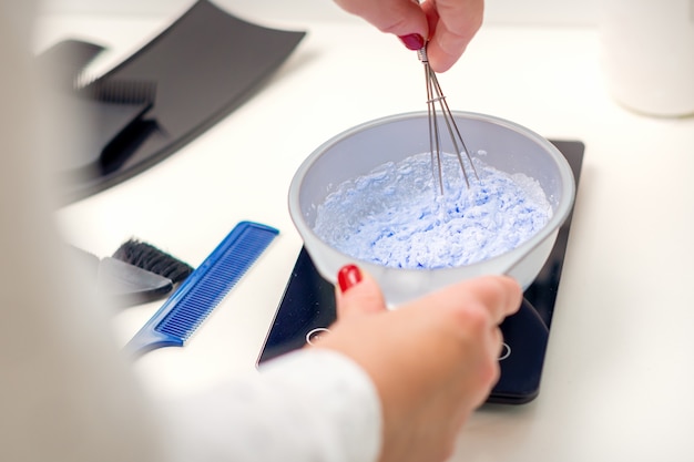 Il parrucchiere sta mescolando la tintura nella ciotola bianca per colorare i capelli nelle sue mani