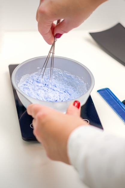 Il parrucchiere sta mescolando la tintura nella ciotola bianca per colorare i capelli nelle sue mani