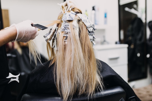 Il parrucchiere sta tingendo i capelli femminili, facendo dei colpi di sole alla sua cliente con una lamina.