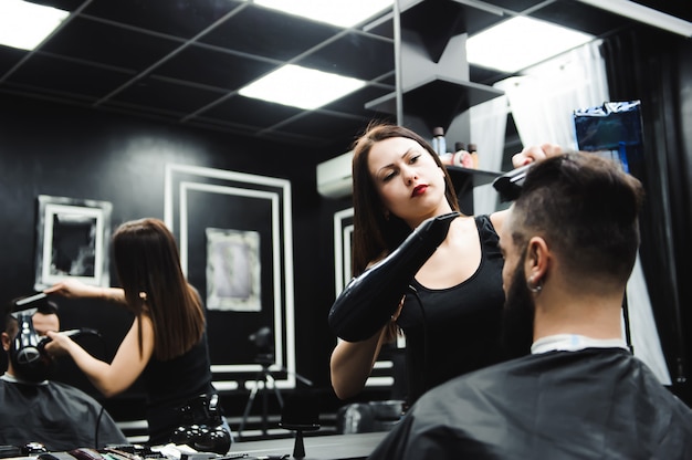 Il parrucchiere taglia i capelli e la barba dell'uomo dal barbiere