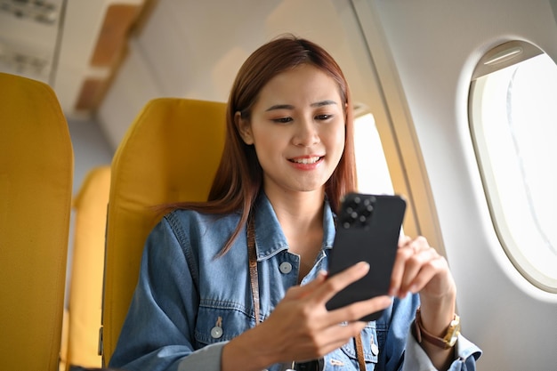 Il passeggero asiatico millenario allegro viaggia in aereo utilizzando lo smartphone