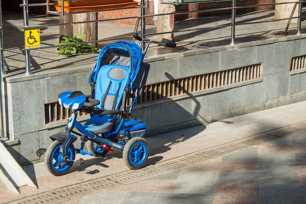 Il passeggiatore del triciclo dei bambini blu sta vuoto nel parcheggio vicino al supermercato