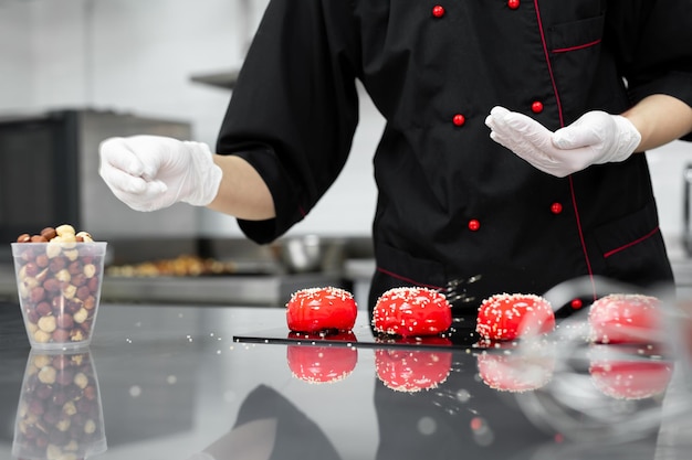 Il pasticcere cosparge la torta di mousse rossa con semi di sesamo.