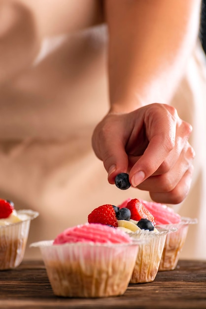 Il pasticcere decora i muffin con frutti di bosco freschi Cupcakes con fragole e mirtilli Cornice verticale Close up