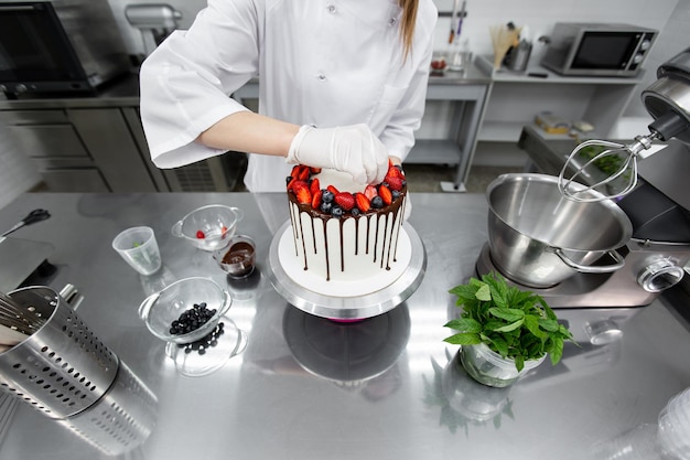 Il pasticcere decora la torta con striature di cioccolato, fragole e mirtilli.