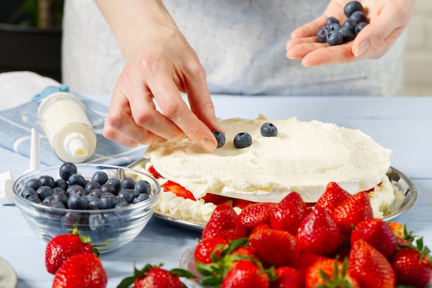 Il pasticcere depone i mirtilli sulla torta di marshmallow alla fragola