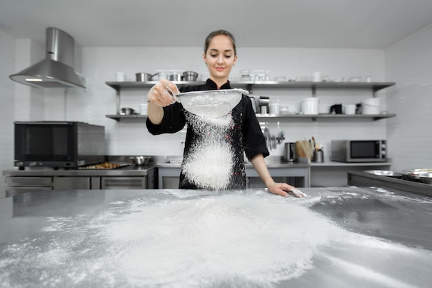 Il pasticcere semina la farina al setaccio sul tavolo.