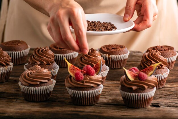 Il pasticcere spruzza con cupcakes al cioccolato con lamponi e fichi Primo piano della preparazione del muffin