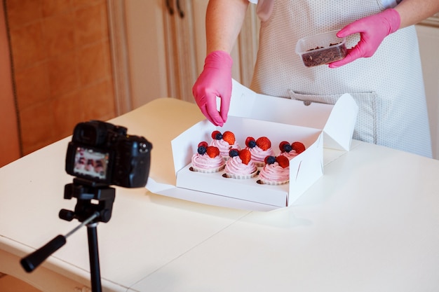 Il pasticcere sta decorando i cupcakes con gocce di cioccolato e lo sta registrando sulla telecamera