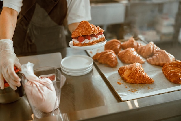 Il pasticcere tiene il croissant con la fragola succosa al bancone di metallo in panetteria