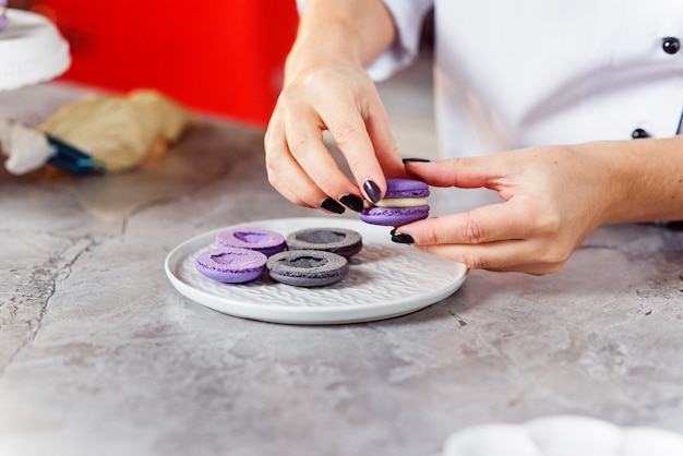 Il pasticcere unisce le parti dei macaron tra loro usando una crema. Chiuda sulle mani del panettiere che producono i macarons.