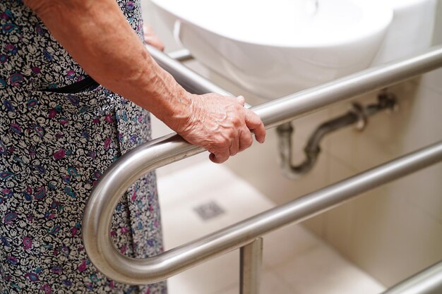 Il paziente asiatico anziano della donna usa la guida di supporto della toilette nella sicurezza della barra di sostegno di sicurezza del corrimano del bagno nell'ospedale di cura