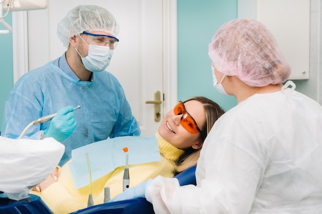 Il paziente sorride sulla poltrona del dentista con una maschera protettiva e uno strumento prima del trattamento nello studio dentistico.