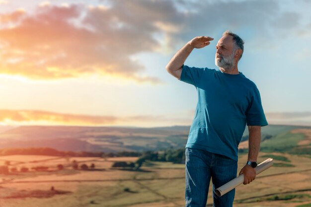 Il pensionato barbuto sta cercando una destinazione sulla mappa sullo sfondo dei campi