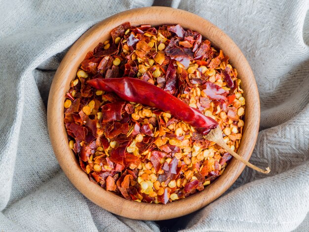 Il peperoncino secco si sfalda in ciotola di legno con l'asciugamano di tela. Frutti secchi e schiacciati di Capsicum frutescens