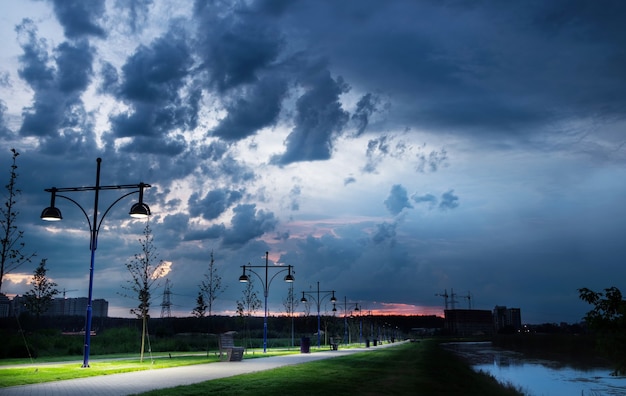 Il percorso del parco cittadino vicino al fiume con lanterne contro il cielo con nuvole di pioggia