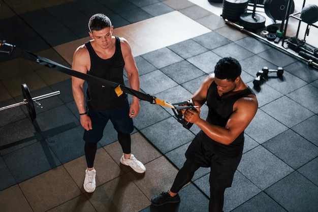 Il personal trainer è al lavoro L'uomo afroamericano con un ragazzo bianco ha una giornata di allenamento in palestra