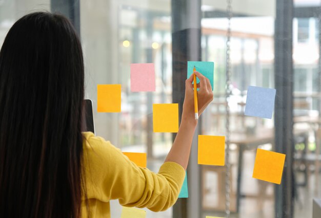 Il personale femminile usa una penna per scrivere un papernote sul vetro per pianificare il proprio lavoro.