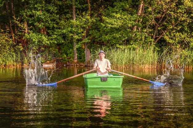 Il pescatore con le canne da pesca sta pescando in una barca di legno sullo sfondo di una natura meravigliosa e di un lago o di un fiume. Turismo in campeggio relax viaggio stile di vita attivo concetto di avventura