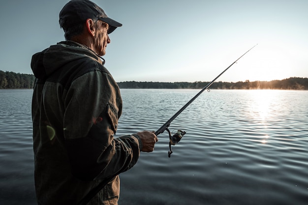 Il pescatore maschio all'alba sul lago pesca una canna da pesca Vacanza di hobby di pesca