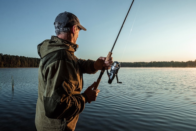 Il pescatore maschio all'alba sul lago pesca una canna da pesca Vacanza di hobby di pesca