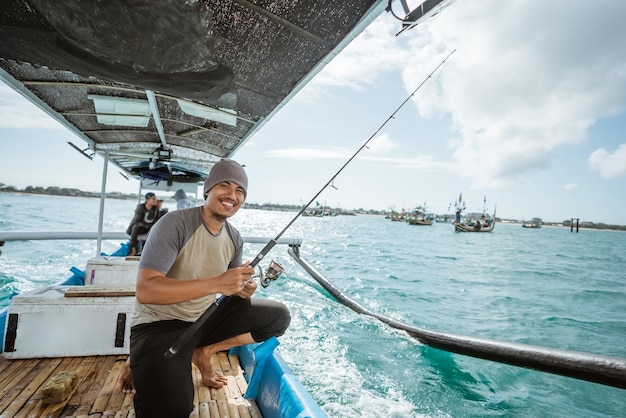 Il pescatore maschio sorridente tiene una canna da pesca mentre parte per la pesca su una piccola barca da pesca