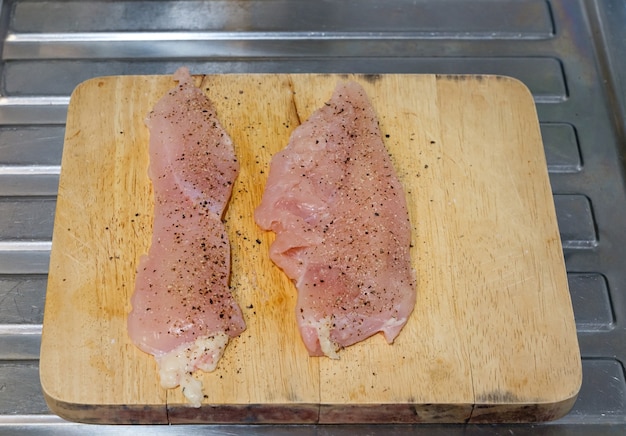 Il petto di pollo fresco con sale e pepe nero sul tagliere di legno pronto da cucinare in cucina, vista del carattere per lo spazio della copia.