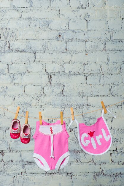 Il pettorale rosa per bambini e le scarpe rosse si asciugano su una corda contro un muro di mattoni bianchi brick
