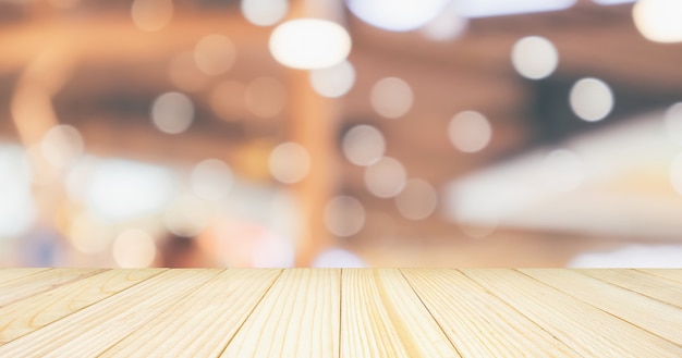 Il piano d'appoggio di legno vuoto con il ristorante del caffè con il bokeh astratto accende il fondo sfocato della sfuocatura