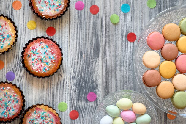 Il piatto pasquale giaceva con macarons, muffin e uova di marzapane in un vassoio decorativo su legno grigio strutturato.