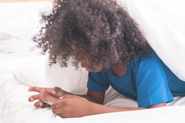 Il piccolo bambino africano sta giocando con lo smartphone sul letto