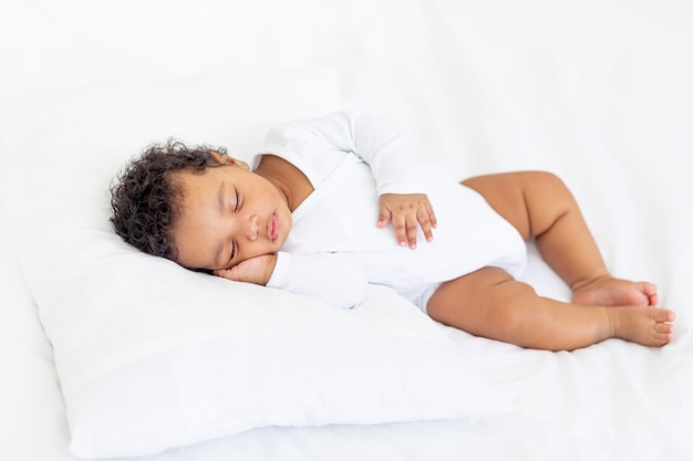 Il piccolo bambino afroamericano dorme su un letto bianco a casa con la mano piegata sotto la guancia