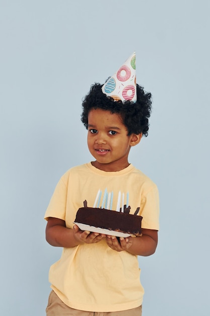 Il piccolo bambino afroamericano felice si diverte al chiuso alla festa di compleanno tiene la torta