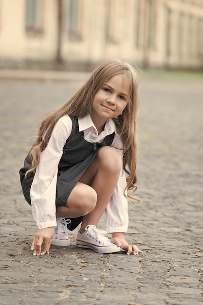 Il piccolo bambino con i capelli lunghi in uniforme scolastica gioca nel cortile della scuola all'aperto infanzia