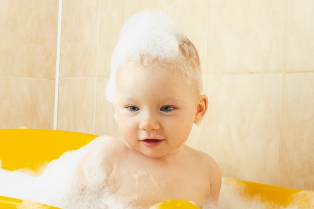 Il piccolo bambino fa il bagno in un bagno giallo con bolle e schiuma.