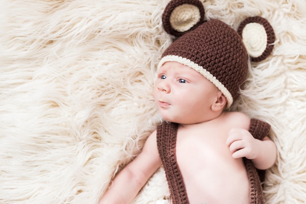 Il piccolo bambino felice sveglio si trova in un costume dell'orso su un bianco. neonato in un cappello con le orecchie su un bianco