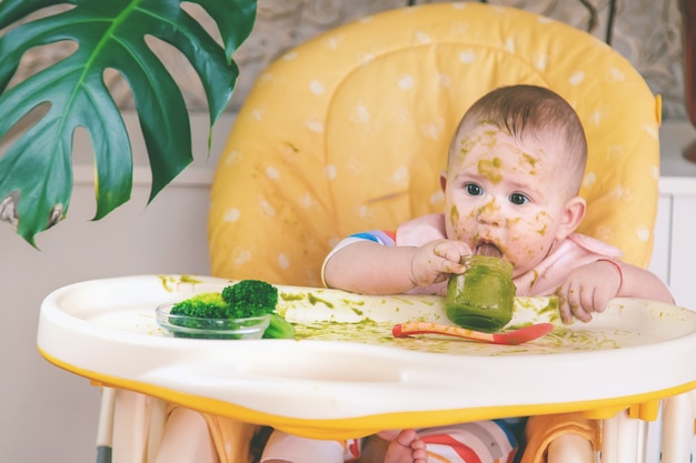 Il piccolo bambino mangia lui stesso la purea di broccoli. Messa a fuoco selettiva. Persone.