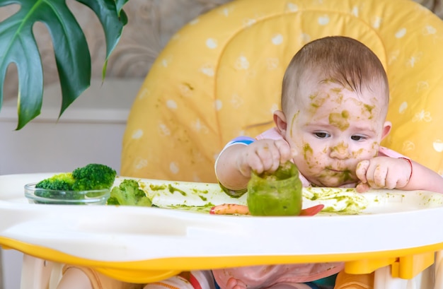 Il piccolo bambino mangia lui stesso la purea di broccoli. Messa a fuoco selettiva. Persone.