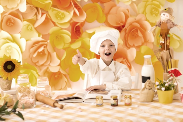 il piccolo bambino prepara piatti deliziosi in cucina e mostra i pollici in su