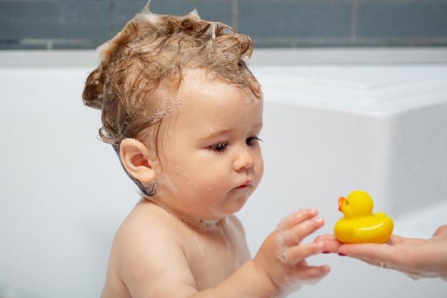 Il piccolo bambino sta lavando i capelli nel bagno di bolle del bambino del bagno