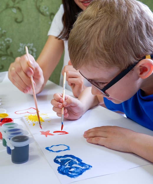 Il piccolo bambino sveglio disegna al tavolo con i colori con sua madre primo piano Sala giochi