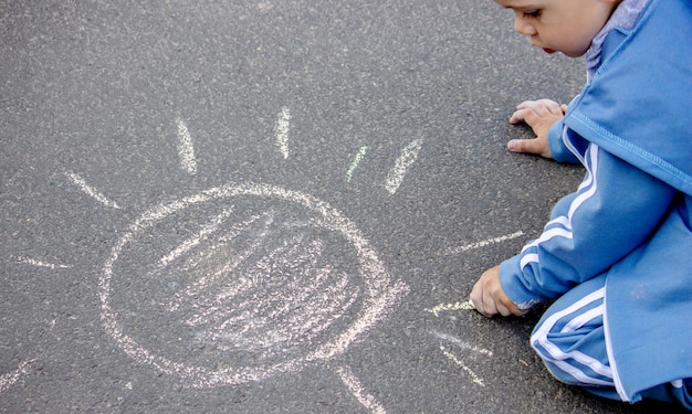 Il piccolo bambino sveglio disegna il sole con il gesso all'aperto