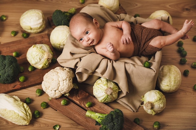 Il piccolo bambino sveglio è sdraiato nella scatola con molti cavoli diversi intorno