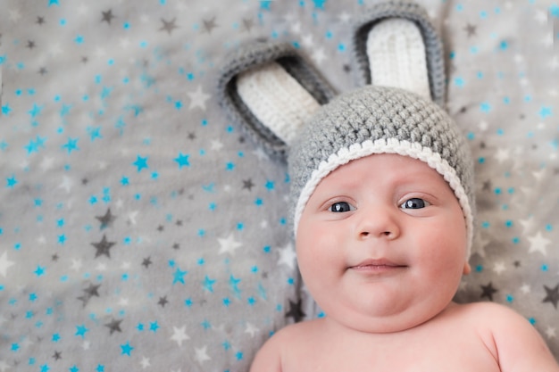 Il piccolo bambino sveglio si trova in un costume della lepre su un bianco. neonato in un cappello con le orecchie su un bianco