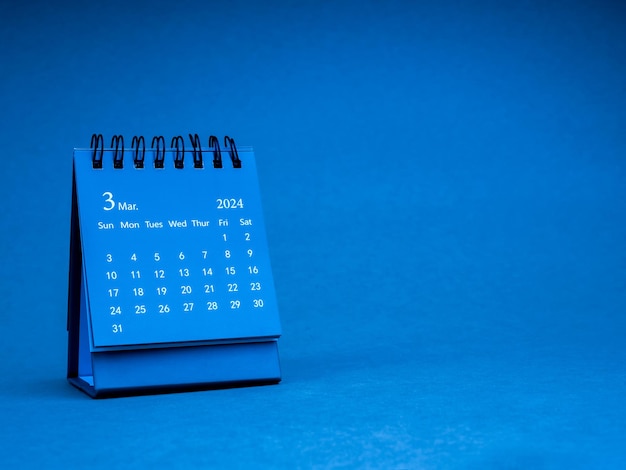 Il piccolo calendario a spirale blu del mese di marzo 2024 per l'organizzatore per pianificare e ricordare isolato su sfondo di carta blu con spazio di copia in stile minimo Calendario a tavola piccola con la pagina del terzo mese