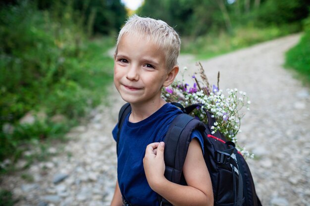 Il piccolo escursionista con lo zaino viene dalla montagna e porta bouquet di fiori di campo bellezza della natura