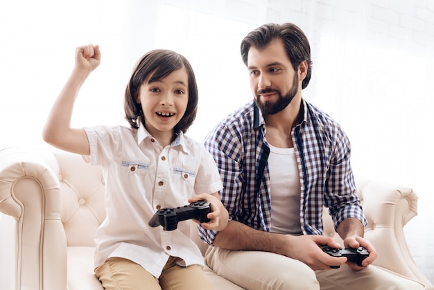 Il piccolo figlio con il joystick si rallegra della vittoria nel gioco con il padre.
