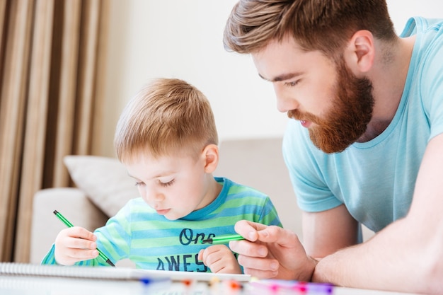 Il piccolo figlio e suo padre disegnano con i pennarelli insieme a casa